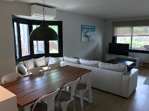 A modern living room with a wooden dining table, white sofa, and a television.