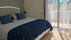 Una cama con cabecera, una lámpara de noche y una ventana con cortinas traslúcidas.