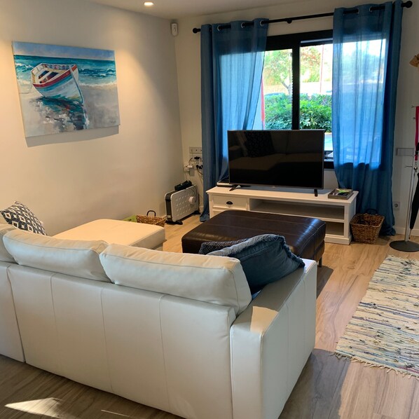 A living room with a white sofa, a flat-screen TV, a coffee table, and a painting of a boat on the wall.