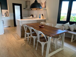 A modern kitchen with white cabinetry, a wooden dining table, white chairs, and a large window with a view.