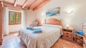 A bedroom with a bed, a nightstand, a chair, a window with curtains, and a painting on the wall. - Holiday Home 'Finca Can Xet' with Mountain View, Pool & Wi-Fi (Felanitx)