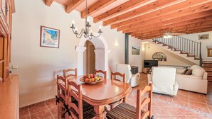 A dining area with a wooden table and chairs, a chandelier, and a staircase leading to another level. - Holiday Home 'Finca Can Xet' with Mountain View, Pool & Wi-Fi (Felanitx)
