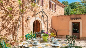 A round table with chairs and a potted plant in an outdoor setting with a stone wall and a door. - Holiday Home 'Finca Can Xet' with Mountain View, Pool & Wi-Fi (Felanitx)