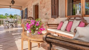 A stone-walled room with a wooden bench, a round table with a vase of flowers, and a view of the outdoors.