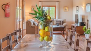A dining table with chairs, a glass vase with fruits, a fire extinguisher, and a window with blinds.