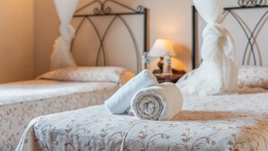 A hotel room with two beds, each with a canopy, a bedside table with a lamp, and rolled towels on the beds.