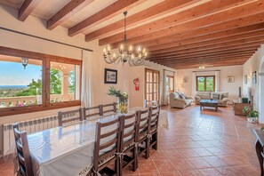 Un comedor con mesa y sillas de madera, una araña y vistas al exterior.