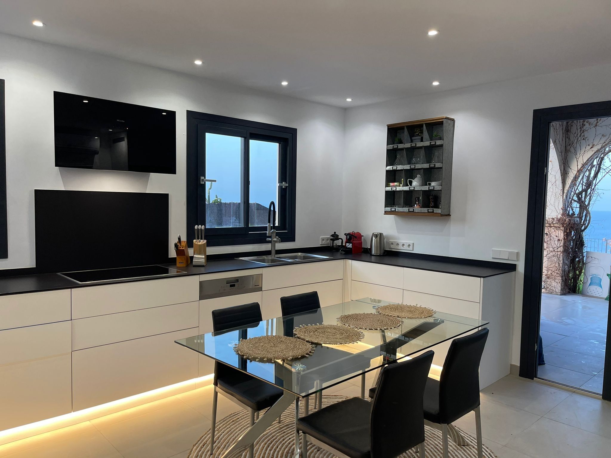 A modern kitchen with a glass dining table, black chairs, and a built-in oven.