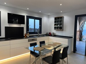 A modern kitchen with a glass dining table, black chairs, and a built-in oven.