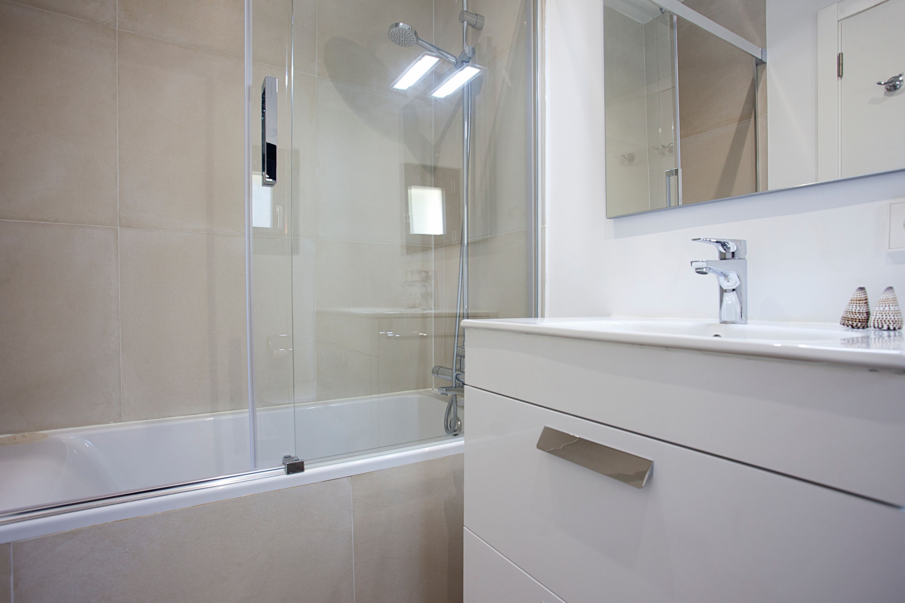 Een moderne badkamer met een douchecabine van glas, een witte wastafel en een spiegel boven het badkamermeubel.