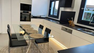 Una cocina moderna con una mesa de vidrio, sillas negras y un horno empotrado.