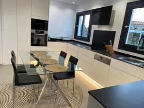 A modern kitchen with a glass dining table, black chairs, and a built-in oven.