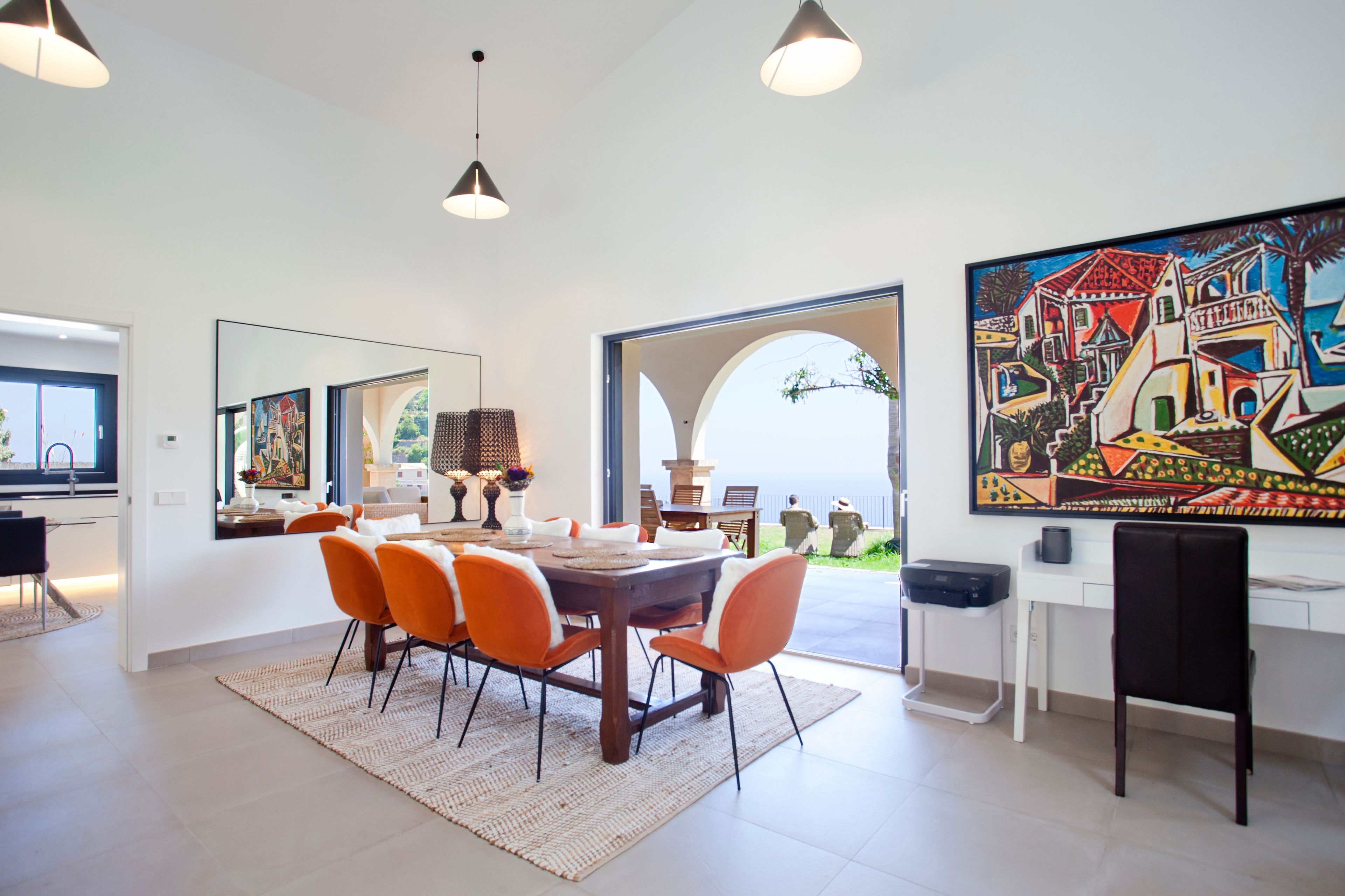 A dining area with a round table, orange chairs, and a large painting on the wall.