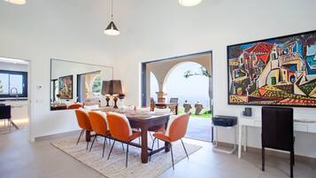 A dining area with a round table, orange chairs, and a large painting on the wall.