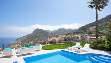 Zona de piscina con sillones de descanso y vista a un pueblo costero.