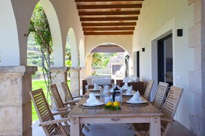 Een terras met een houten tafel voor vier personen, omringd door rieten stoelen.