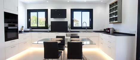 Cocina moderna con una isla central, dos sillas negras, una mesa de vidrio y un televisor empotrado sobre la isla.
