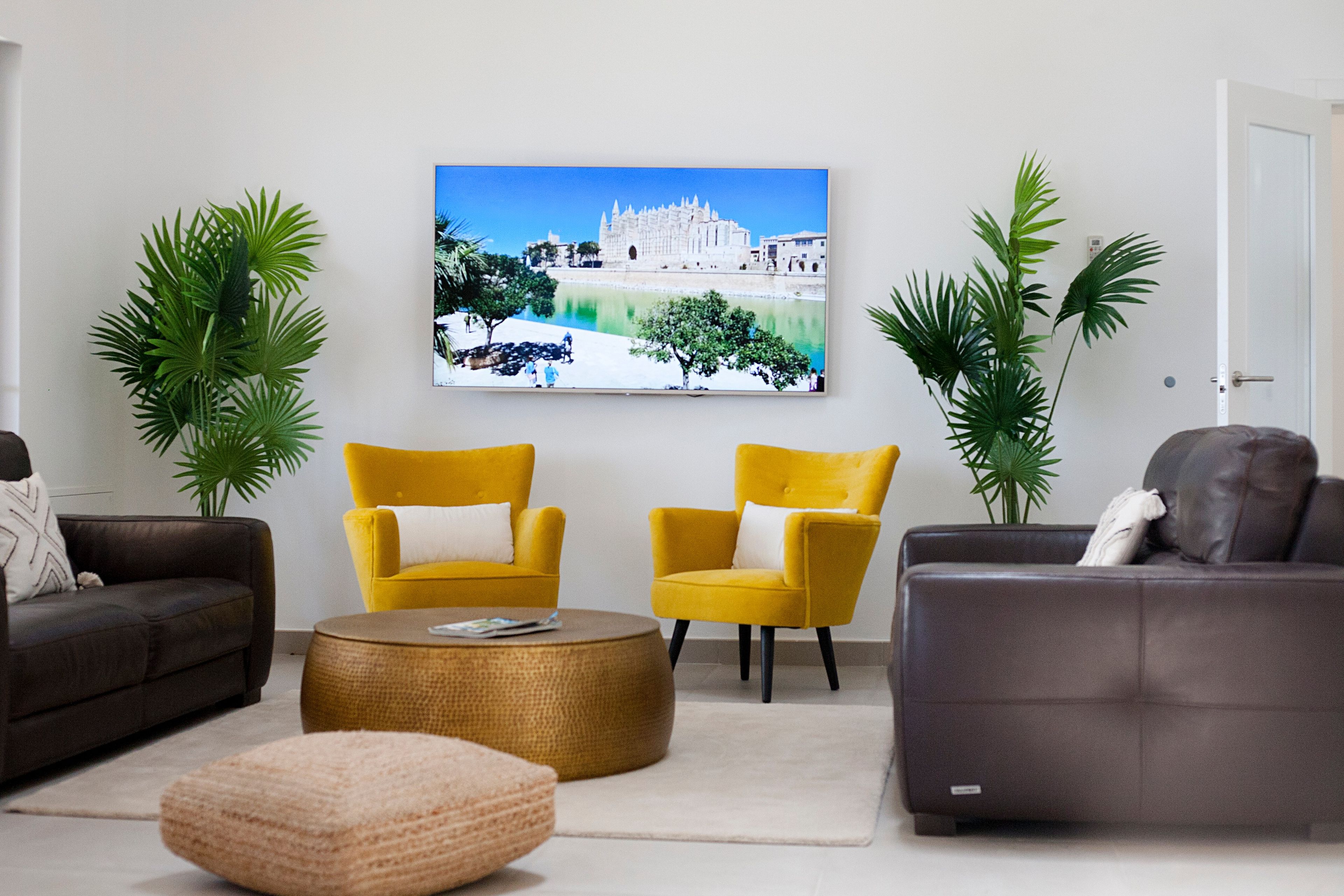 A living room with two yellow armchairs, a grey sofa, a round coffee table, and a painting of a building on the wall.