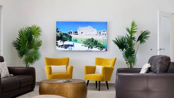 A living room with two yellow armchairs, a grey sofa, a round coffee table, and a painting of a building on the wall.