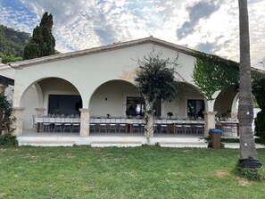 A building with a covered outdoor dining area, multiple arches, and a grassy lawn.