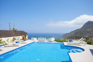 A swimming pool with lounge chairs and a view of the sea.