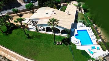 Vista aérea de una propiedad con piscina, múltiples sillas de descanso y un césped bien cuidado.