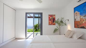 A bedroom with a large bed, a sliding glass door leading to a balcony, and a painting on the wall.