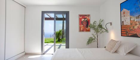 Un dormitorio con una cama grande, un ventanal corredero que da a un balcón y un cuadro en la pared.