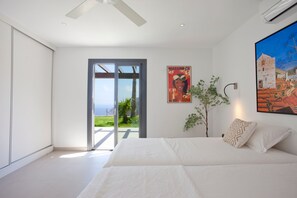A bedroom with a large bed, a sliding glass door leading to a balcony, and a painting on the wall.