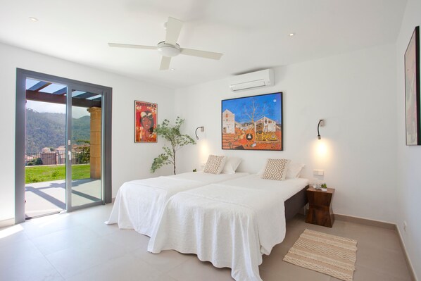 A bedroom with a bed, a nightstand, a lamp, a ceiling fan, and a window with a view of a landscape.