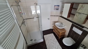 Een badkamer met een douchecabine van glas, een witte wastafel, een houten opbergmeubel en een toilet.