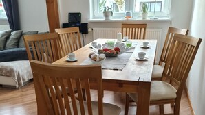 Een eetgedeelte met een houten tafel en stoelen, een raam met zonwering, en uitzicht op de omgeving.