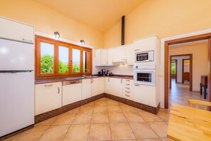 A kitchen with white cabinets, a microwave, oven, and a window with a view of greenery. - Holiday home 'Finca Ca'n Terrasa' with Mountain View, Pool & Wi-Fi (Capdepera)