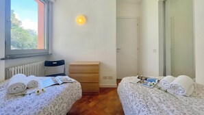 A bedroom with two beds, a window, a radiator, a bedside table, a mirror, and a door. - Gaeta 'lake View' (San Siro)
