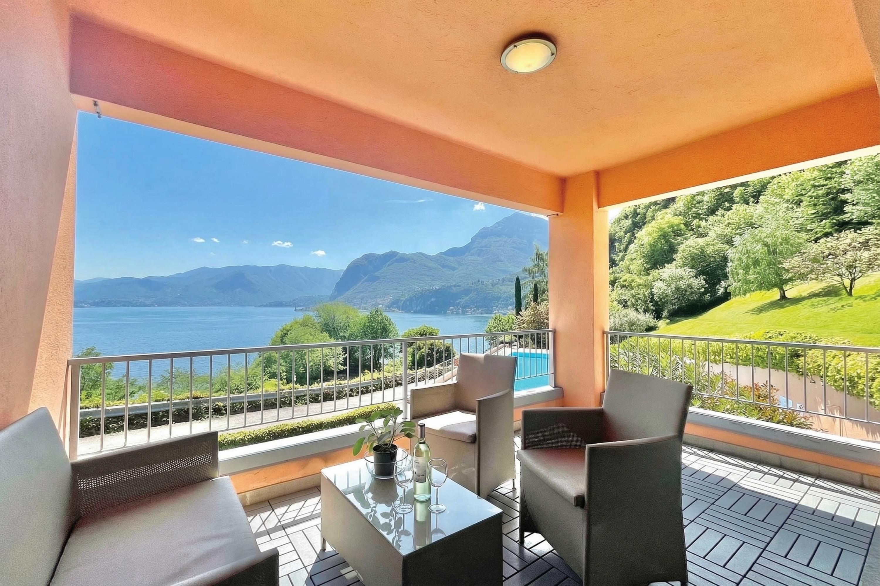 A balcony with a table, chairs, and a view of a lake and mountains.