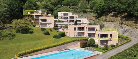 Un hotel en una ladera con piscina, varios balcones y abundante vegetación.