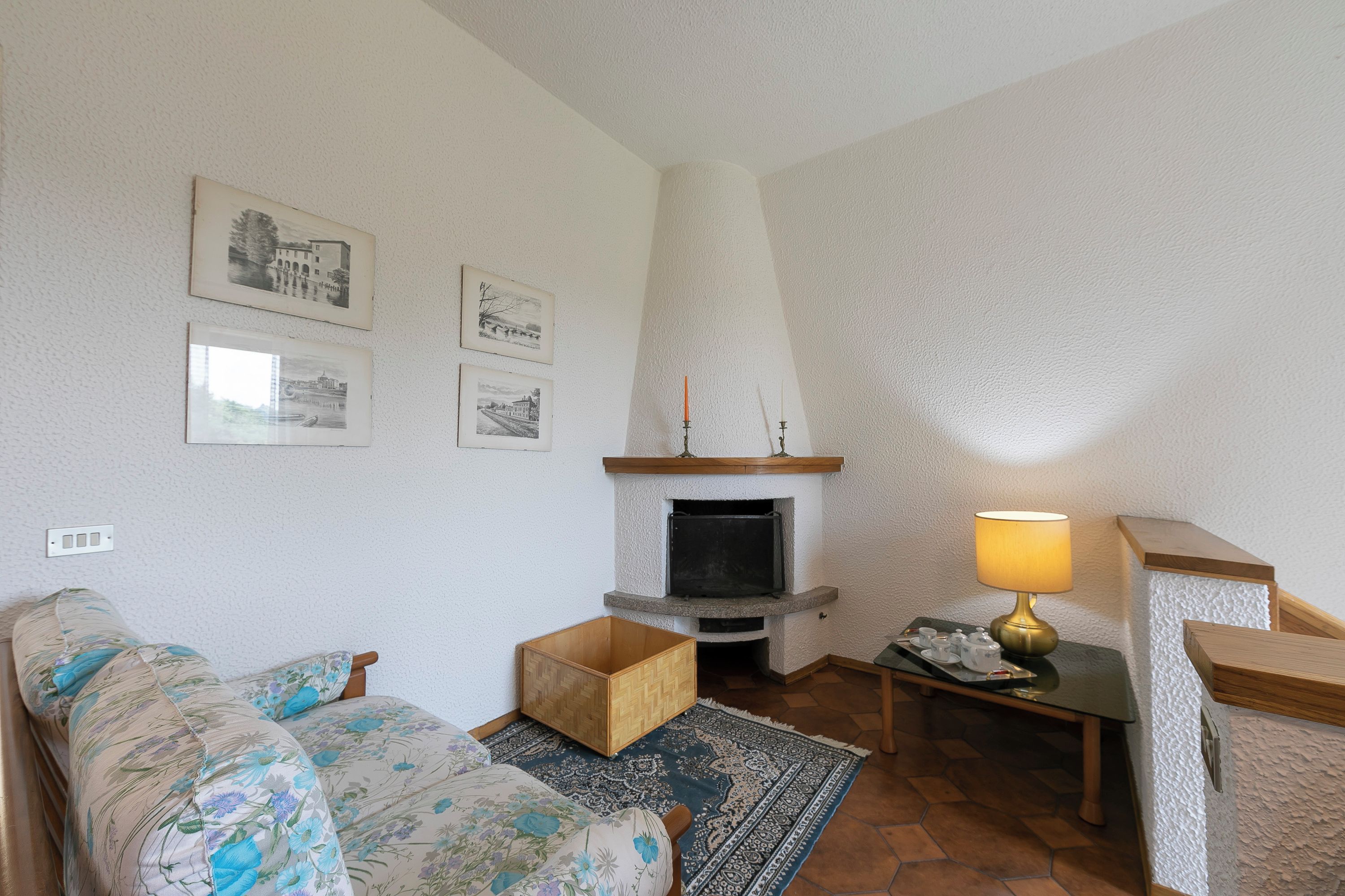 Ein Wohnzimmer mit einer Couch, einem Kamin, einer Lampe und gerahmten Bildern an der Wand.