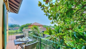 Un balcon agrémenté de meubles en osier, une table mise avec une théière et des tasses, et une vue sur une maison au loin.