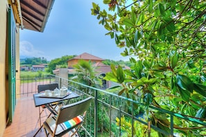 A balcony with wicker furniture, a table set with a teapot and cups, and a view of a house in the background.