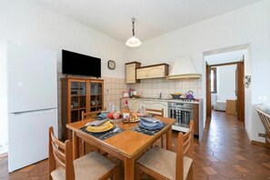 Ein Essbereich mit Holztisch und Stühlen, einem Fernseher über dem Tisch und einer Küche im Hintergrund.