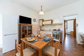 Une cuisine compacte avec un coin repas, un téléviseur fixé au-dessus du comptoir et une horloge visible au mur.