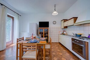 A kitchen with a dining table set, a TV, cabinets, and a stove. - Charming La Gelosia Few Min From Lake: 2BR Monvalle Apartment (Monvalle)