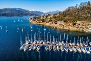 A marina with numerous sailboats docked, a mountainous backdrop, and buildings along the shore.