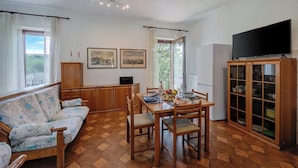 Un coin repas avec une table et des chaises en bois, un canapé, un meuble avec des portes en verre et un téléviseur fixé au mur.