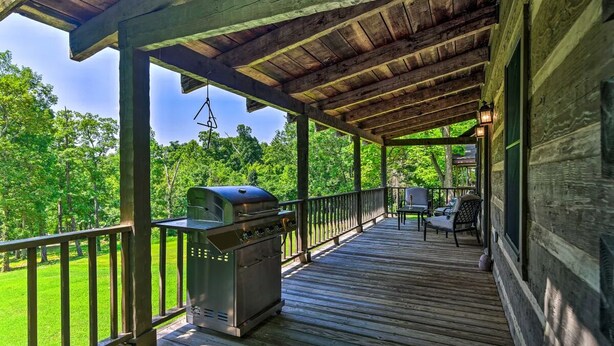A covered porch with a grill, outdoor furniture, and a view of a green landscape. - Cozy Roughriver Lakefront Cabin (McDaniels)