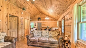 A log cabin interior with a wooden ceiling, a leather sofa, and a dining area with a table and chairs. - Cozy Roughriver Lakefront Cabin (McDaniels)