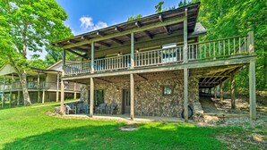 A two-story wooden cabin with a balcony, stone walls, and outdoor seating. - Cozy Roughriver Lakefront Cabin (McDaniels)