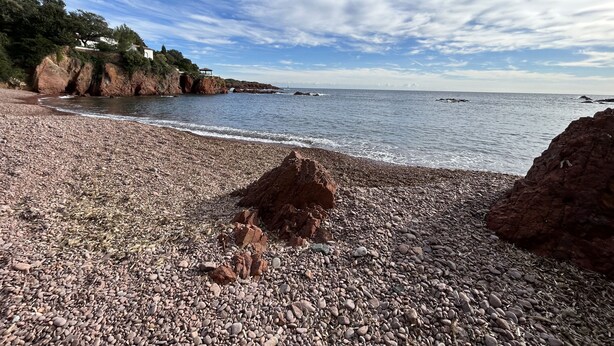 En strand med småsten och klippformationer, och en klar himmel.