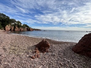 Una playa pedregosa con afloramientos rocosos y cielo despejado.