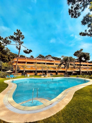 Relax by the inviting pool surrounded by lush greenery and a modern building in the background.